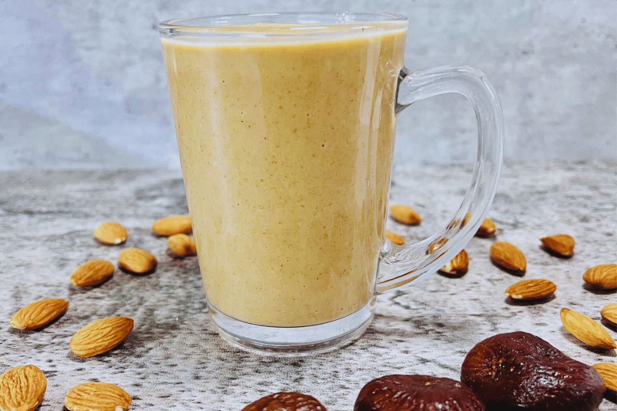 A brown smoothie served in a tall glass, surrounded by almonds and dried figs