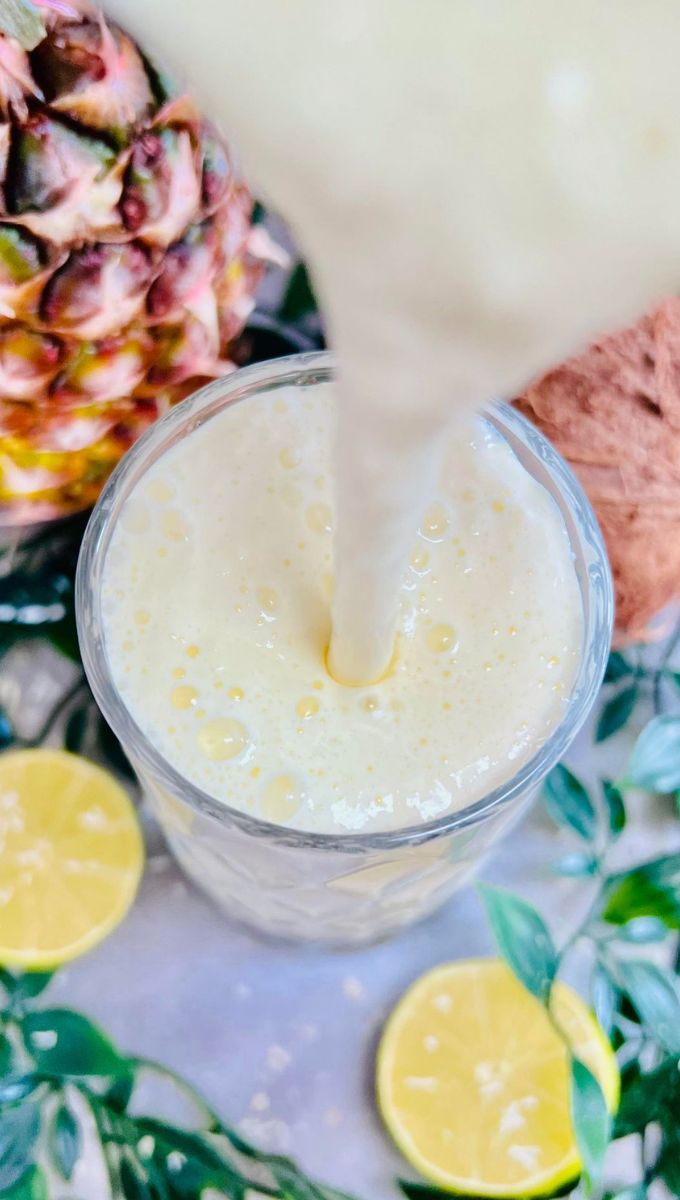Pina Colada Smoothie being poured into a glass cup from a blender jug