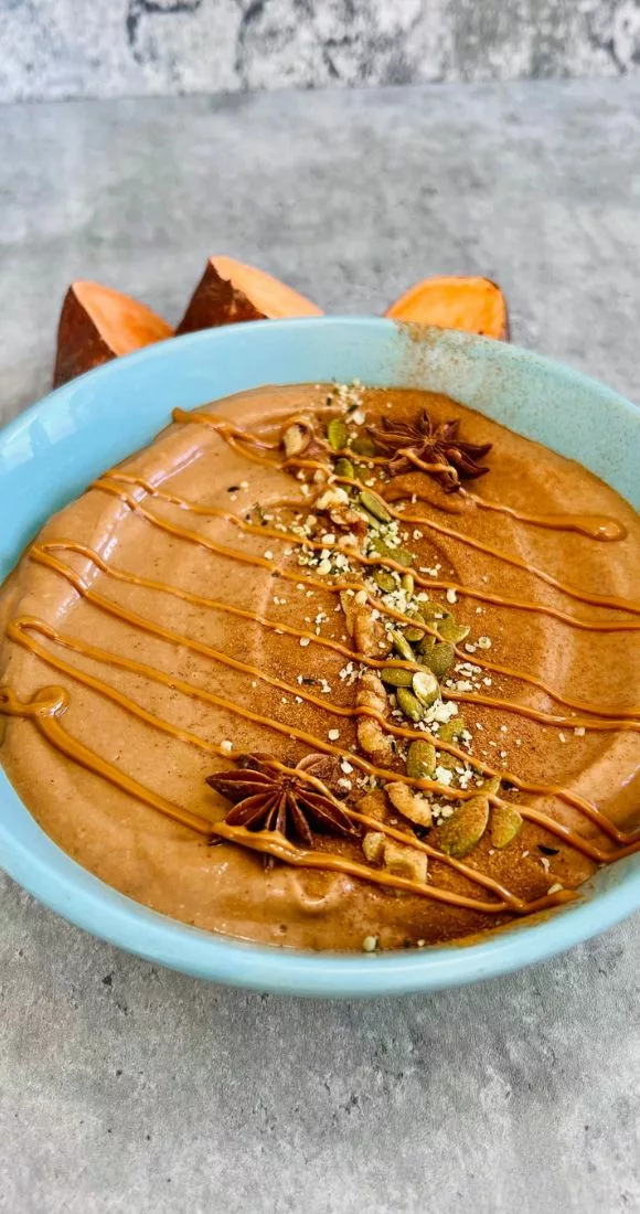 a side shot of a blue bowl filled with sweet potato smoothie topped with nuts and a drizzle of peanut butter