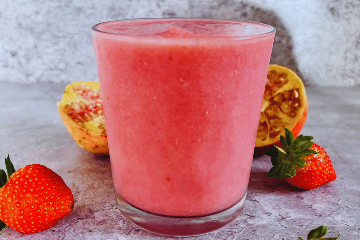 A pink smoothie made with strawberries and grapefruit served in a glass cup