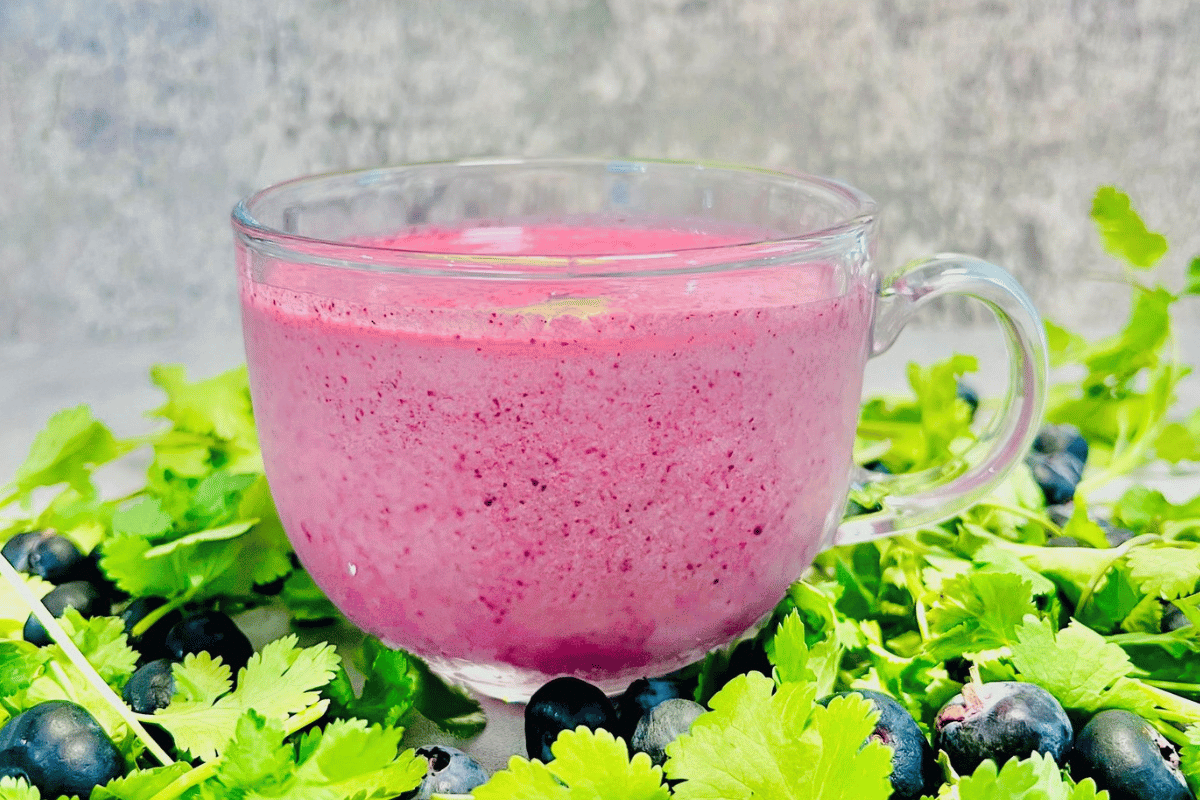 glass cup filled with a smoothie surrounded by fresh blueberries and cilantro
