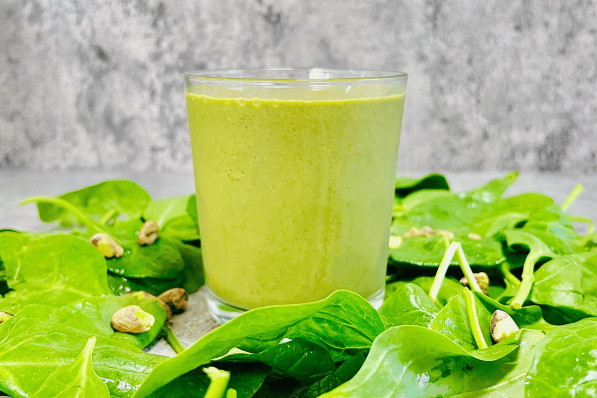 glass-cup-filled-with-a-smoothie-surrounded-by-fresh-spinach-and-pistachio-nuts