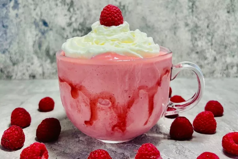 a glass cup filled with a strawberry dessert smoothie topped with whipped cream-min