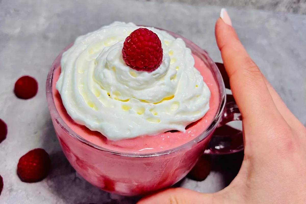 a hand holding a glass cup of strawberry smoothie topped with whipped cream-min