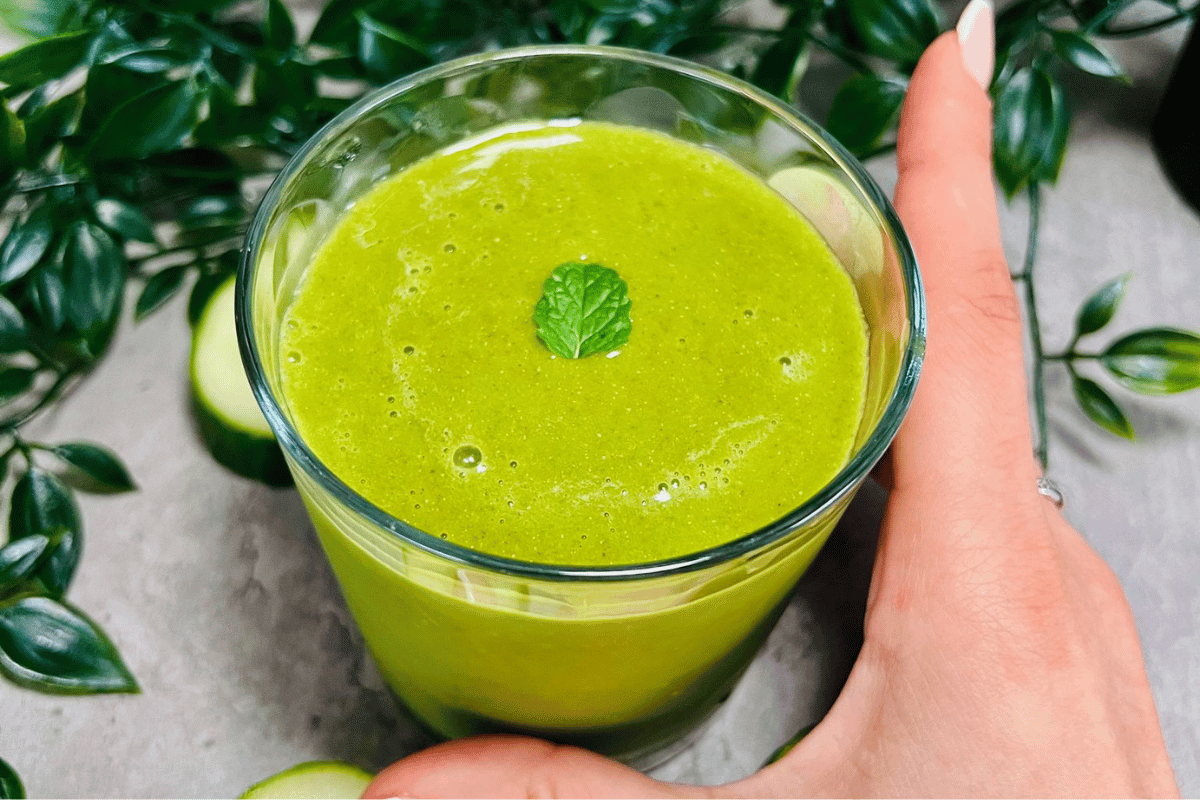 a-hand-holding-a-glass-cup-filled-with-a-green-detox-pineapple-smoothie