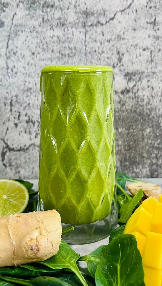 a tall glass cup filled with a green mango smoothie