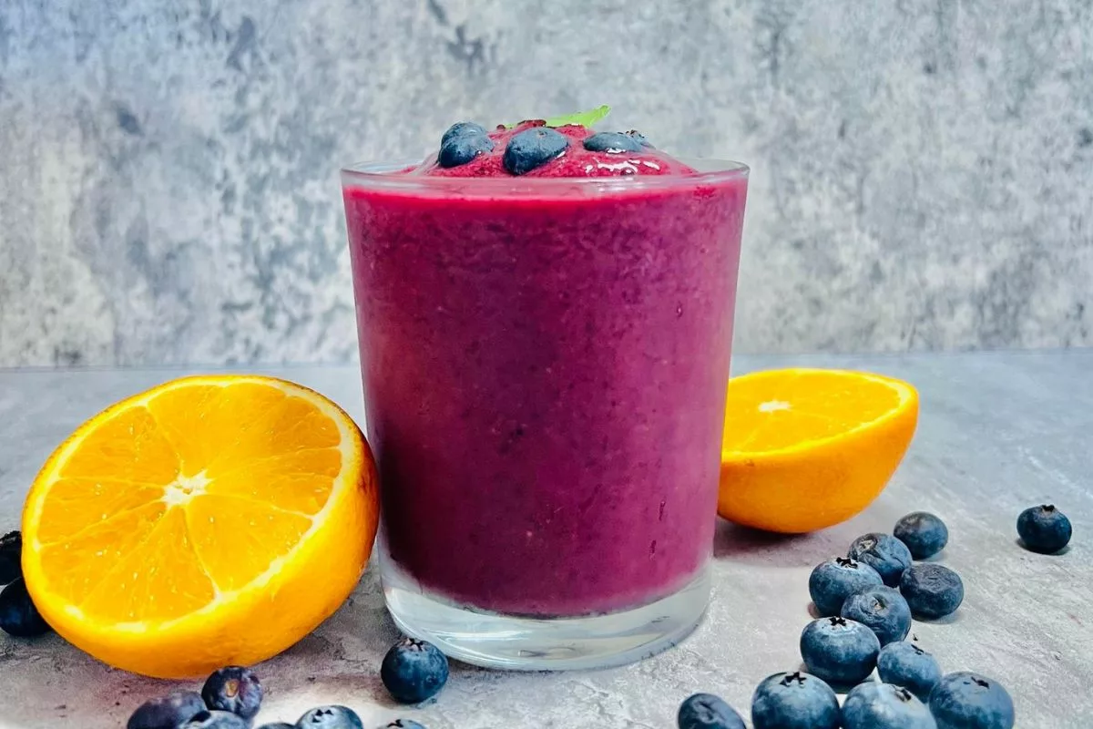 glass cup filled with blueberry smoothie surrounded by fresh orange and blueberries
