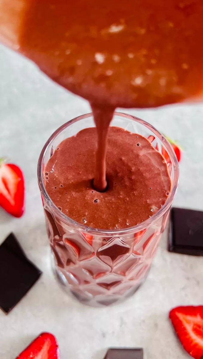 Chocolate Strawberry Smoothie being poured into a tall thick glass cup from a blender jug
