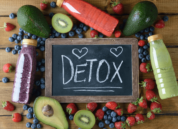 A board that has detox written on it with smoothies and fruit