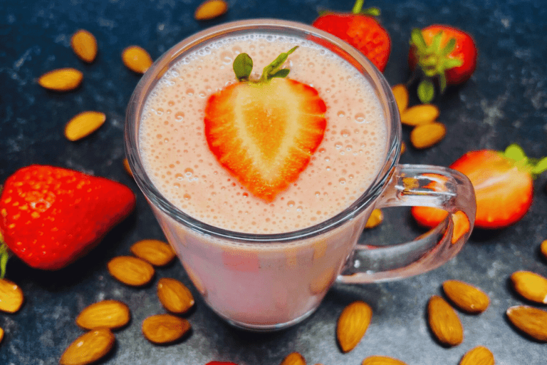 Smoothie For Upset Stomach served in a tall glass cup surrounded by fresh strawberries and almonds