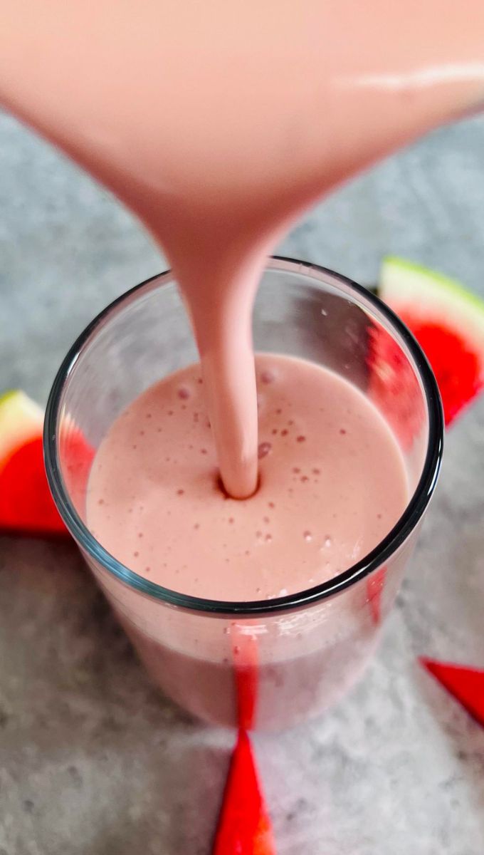 Watermelon Protein Smoothie being poured into a tall thin glass cup from a blender jug