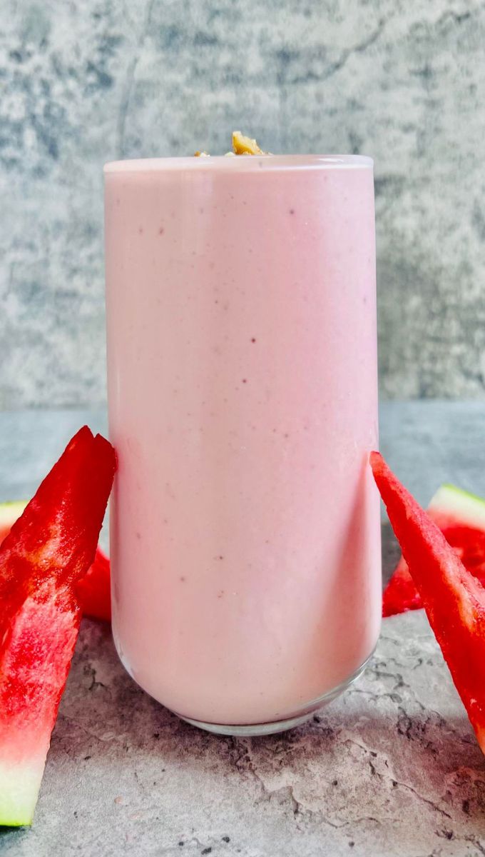 Watermelon Protein Smoothie served in a tall thin glass cup surrounded by slices of fresh watermelon