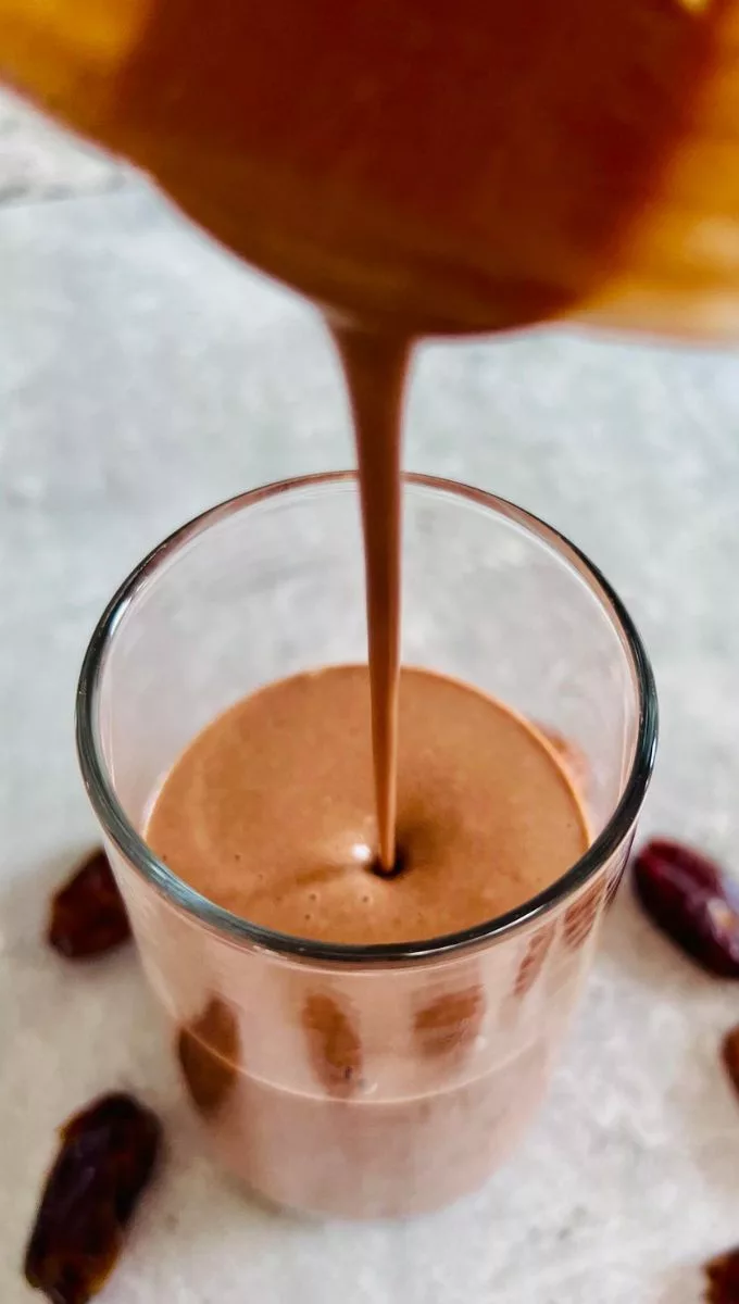 chocolate smoothie being poured from a blender to a tall thin glass cup