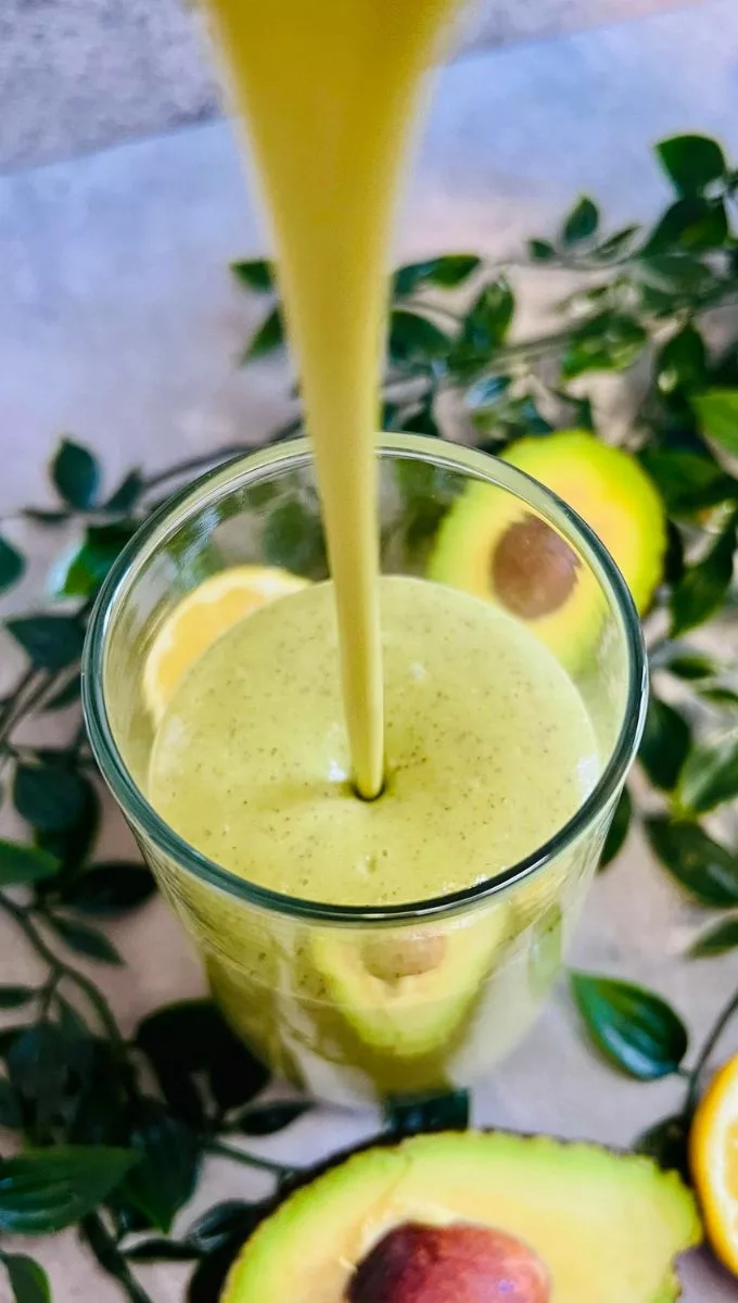 Avocado Matcha Smoothie being poured into a tall thin glass cup from a blender jug