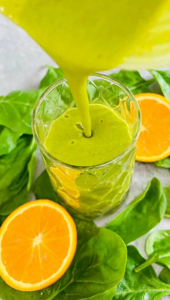Orange Spinach Smoothie being poured into a thick glass cup from a blender