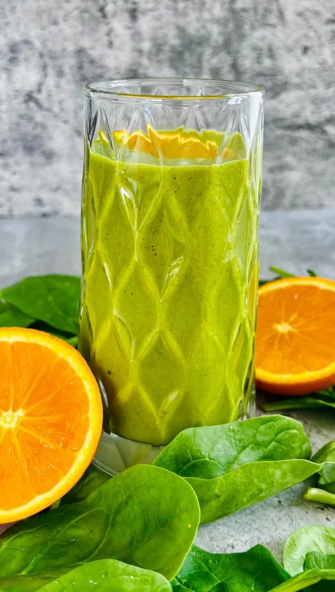 Orange Spinach Smoothie served in a thick glass cup surrounded by fresh spinach and sliced orange