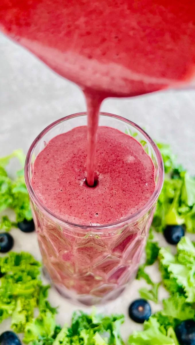 Kale Blueberry Kefir Smoothie being poured into a tall thick glass cup from a blender jug