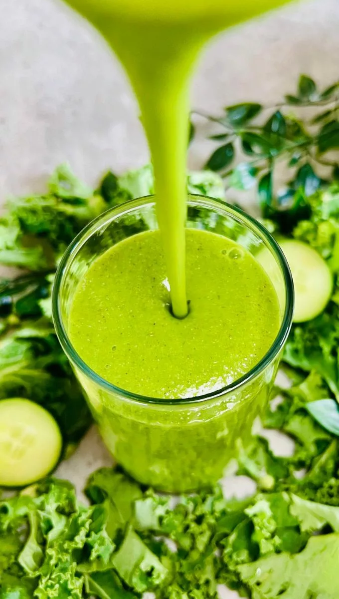 Kale Cucumber Smoothie being poured into a thin glass cup from a blender jug