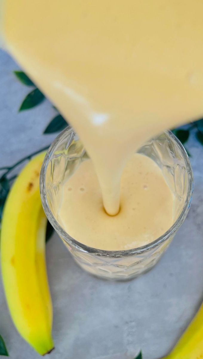 Mango Banana Smoothie being poured into a thick tall glass cup from a blender jug
