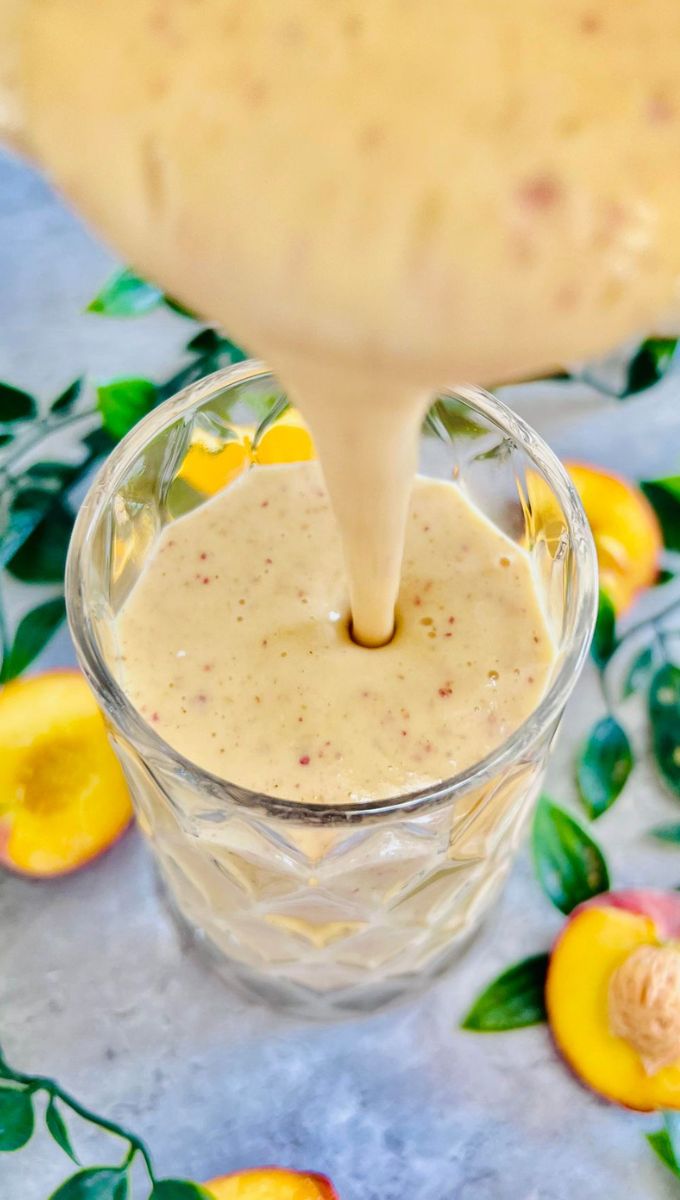 Peach Smoothie With Yogurt being poured into a tall thick glass cup from a blender jug