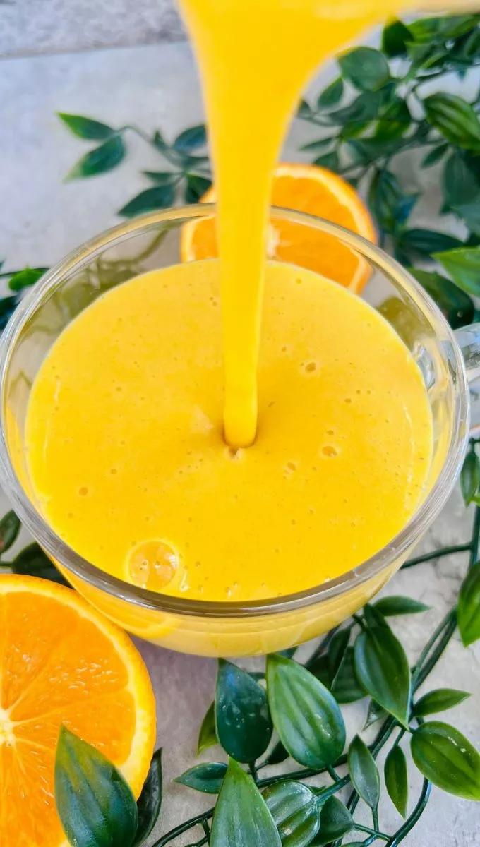 Anti-Inflammatory Orange And Turmeric Smoothie being poured into a round glass cup from a blender jug