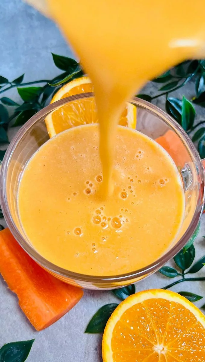 Carrot Orange Ginger Smoothie being poured into a round glass cup from a blender jug