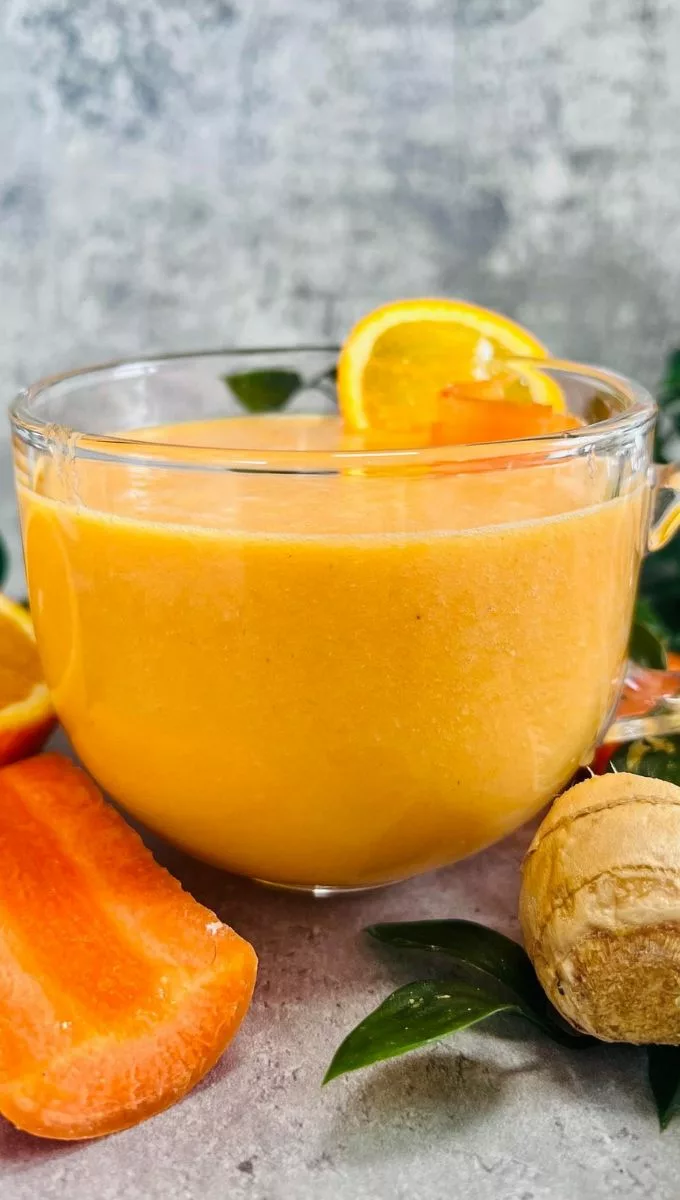 Carrot Orange Ginger Smoothie served in a round glass cup surrounded by sliced orange and carrot