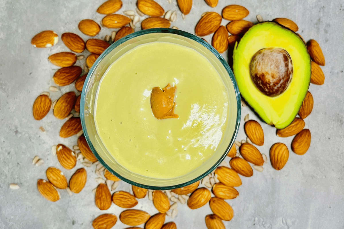 Keto avocado smoothie served in a glass cup surrounded by almonds