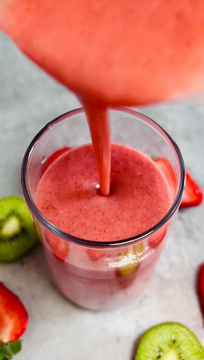 Strawberry Kiwi Smoothie being poured in a tall thin glass cup from a blender jug