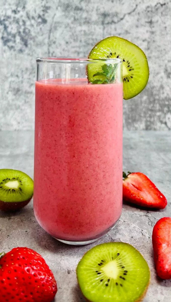 Strawberry Kiwi Smoothie served in a tall thin glass cup surrounded by sliced strawberries and kiwi