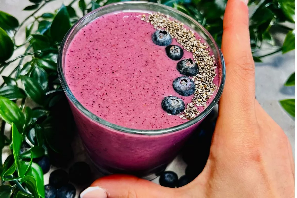a hand holding a glass cup of Blueberry Protein Smoothie