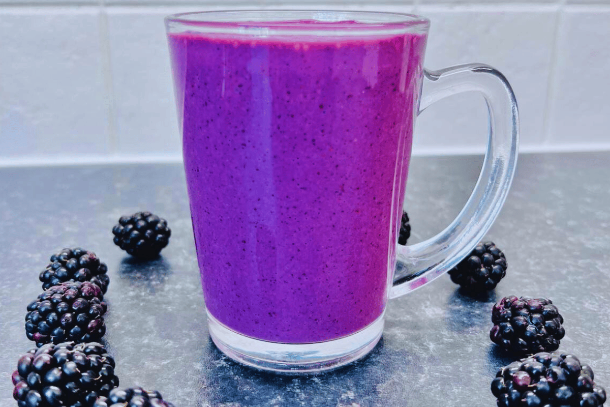 a Blackberry Smoothie For Weight Loss poured into a glass cup surrounded by fresh blackberries