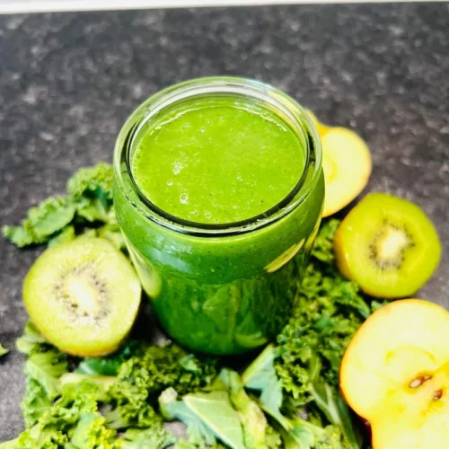 Green smoothie surrounded by kiwi, kale and apple