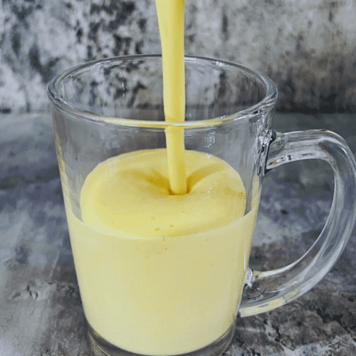2 ingredients mango smoothie being poured into a tall glass cup