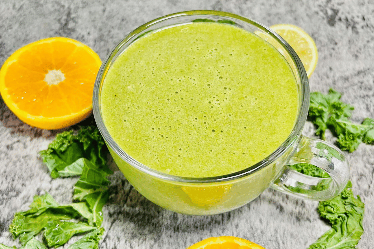Alcohol Detox Smoothie served in a tall glass cup, the cup is surrounded by sliced orange and fresh kale