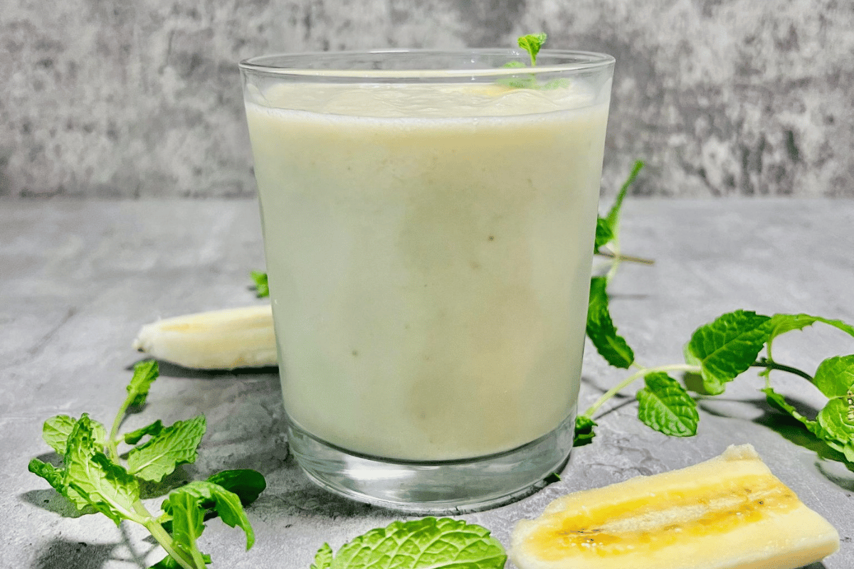 sliced banana and fresh mint around a glass cup filled with a smoothie