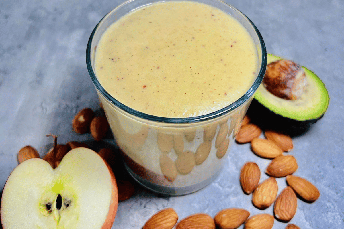apple avocado and almonds around a glass cup filled with a smoothie