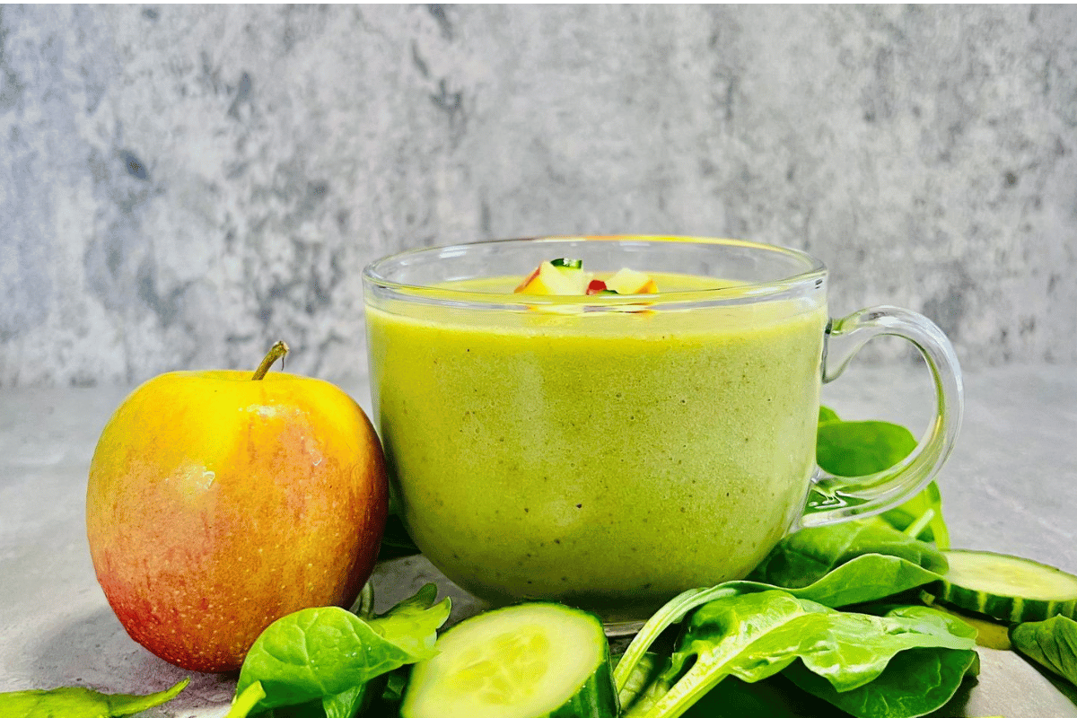 Cucumber Apple Smoothie filled into a glass cup surrounded by fresh apple sliced cucumber and spinach