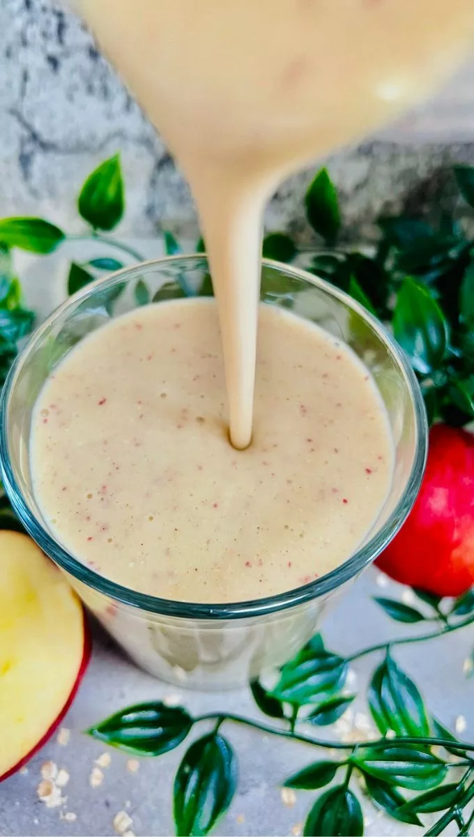 apple oatmeal smoothie being poured into a glass cup from a blender