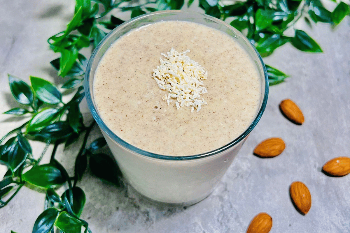 banana smoothie with coconut oil surrounded by a green plant and almonds