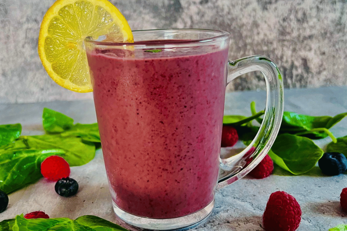 filled glass cup with smoothie, surrounded by berries and spinach