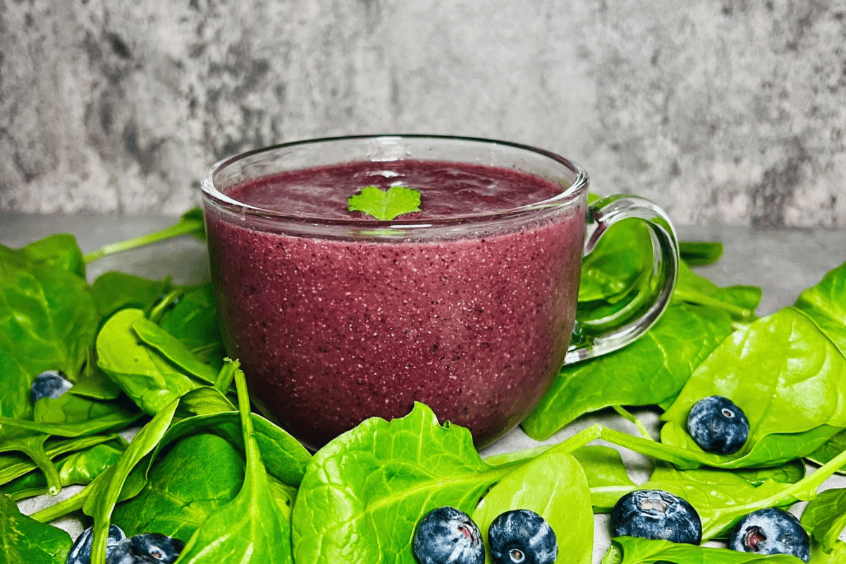 glass cup filled with a fennel and berry smoothie surrounded by spinach and blueberries