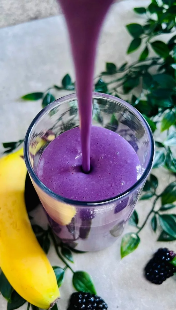 Banana Blackberry Smoothie being poured into a thin tall glass cup