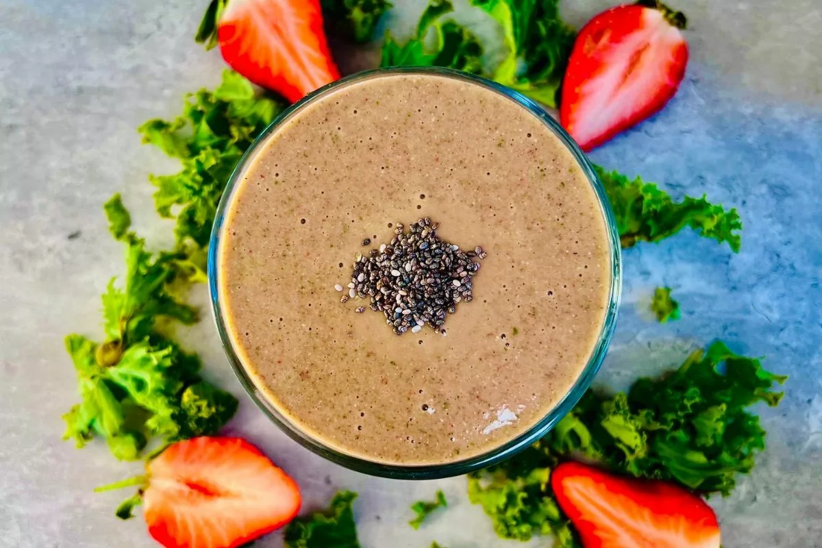 Kale Banana Strawberry Smoothie topped with chia seeds surrounded by fresh kale and strawberries