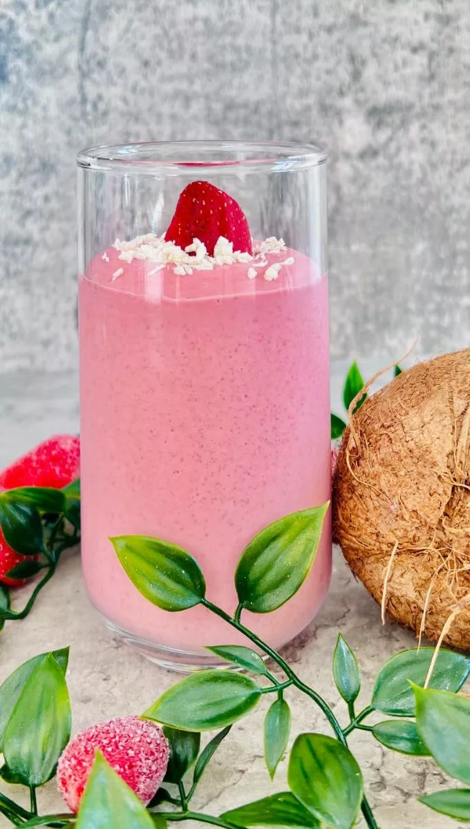 Strawberry Coconut Milk Smoothie surrounded by strawberries a whole coconut and greens