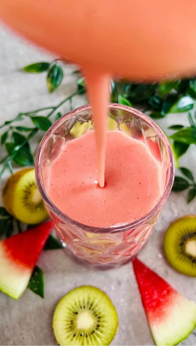 Watermelon Kiwi Smoothie being poured into a tall thick glass cup from a blender jug