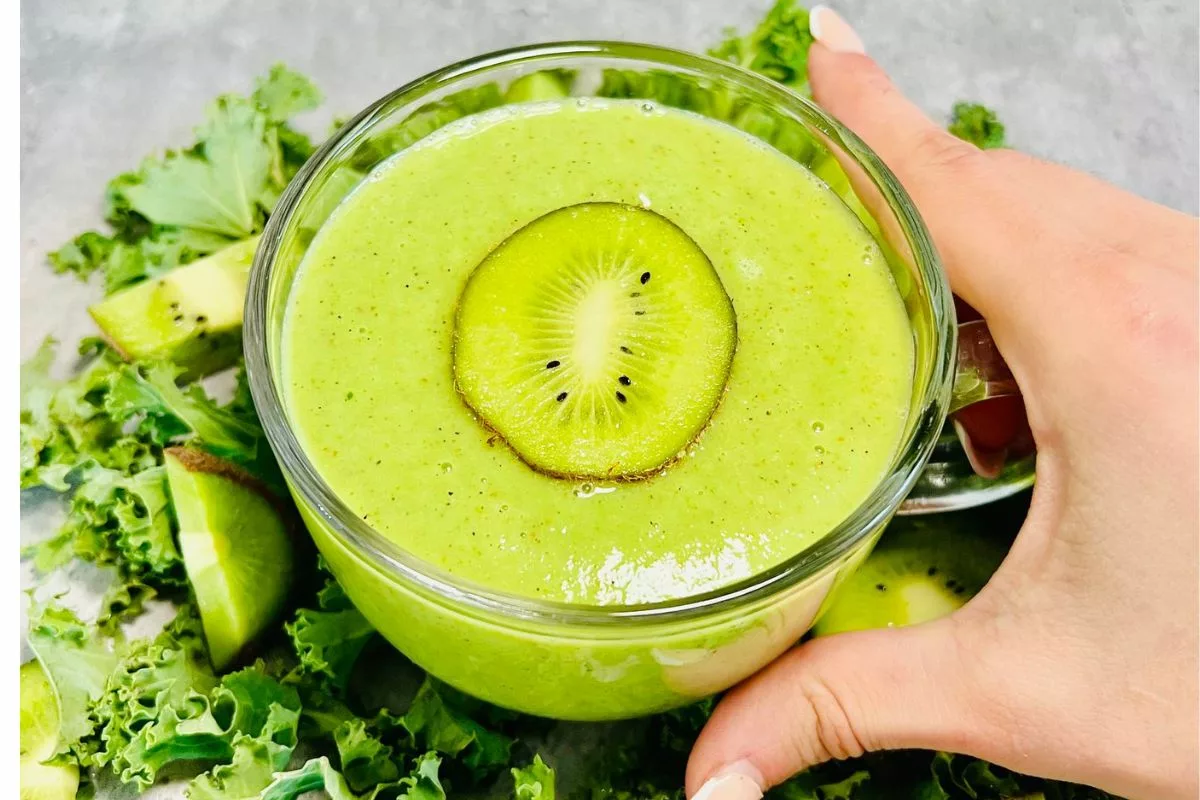 a hand holding a glass cup filled with a green smoothie topped with a slice of kiwi (1)