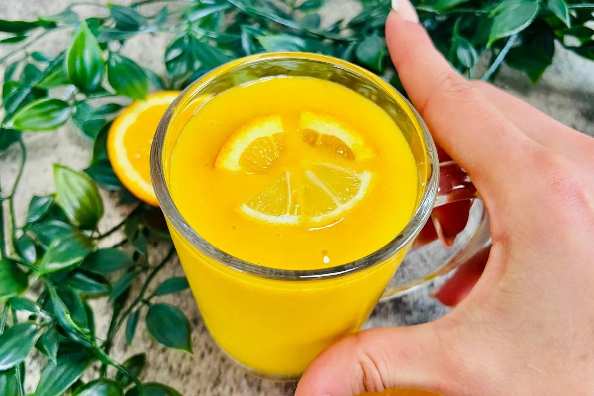 a hand holding a glass cup filled with orange smoothie