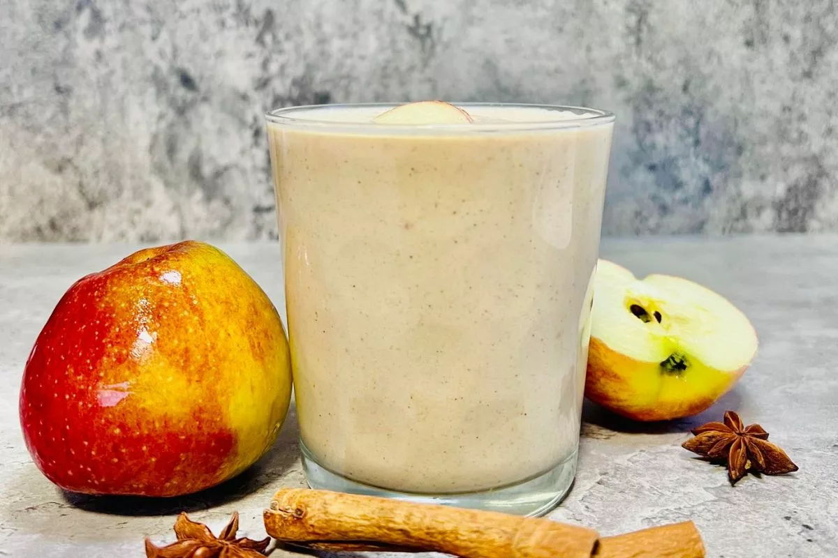 a side shot of Apple Pie Protein Smoothie surrounded by apple and cinnamon sticks