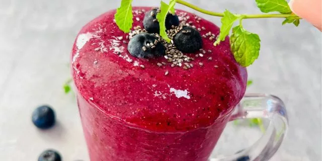 a side shot of a glass cup filled with a smoothie topped with blueberries